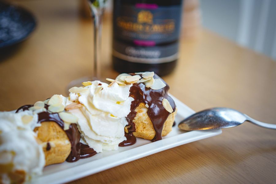Profiteroles au chocolat et chantilly, une bouteille en arrière-plan