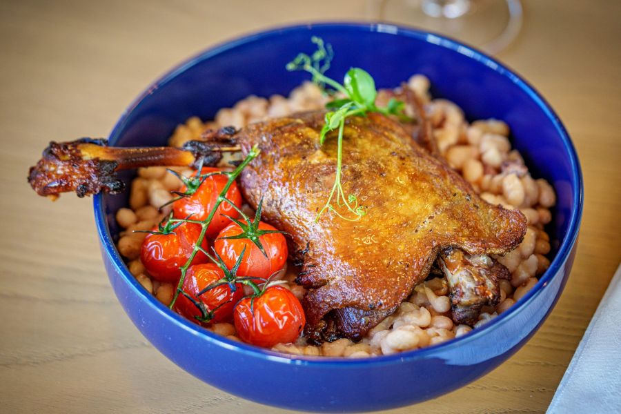 Cuisse de canard sur haricots blancs et tomates cerises, dans un bol bleu